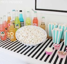 a table topped with popcorn and drinks next to cupcakes on top of a black and white striped table cloth