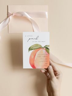 a person holding up a card with an orange on it and a pink ribbon around it