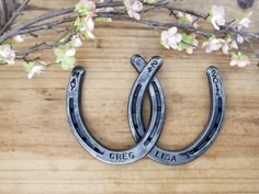 two metal horseshoes sitting on top of a wooden table next to branches with flowers