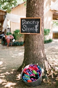 a bucket full of colorful shoes under a tree with a chalkboard sign on it