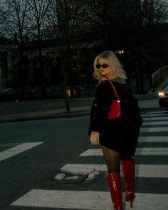 a woman in red boots is walking across the street