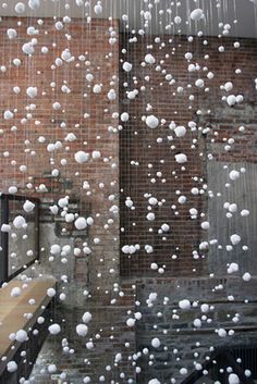 snow is falling from the roof of a building in front of a brick wall and window