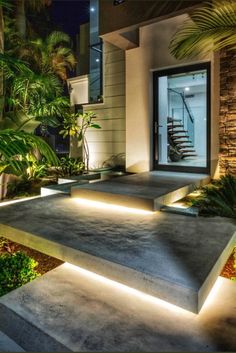 a house with steps lit up and plants in the foreground, along with palm trees on either side