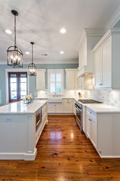 a large kitchen with white cabinets and wood flooring, along with a chandelier hanging from the ceiling