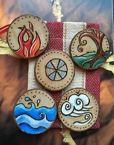 four wooden buttons with designs on them sitting on a piece of cloth next to a tree