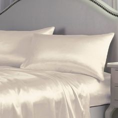 a bed with white sheets and pillows on top of it next to a night stand