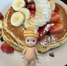 a plate with pancakes, strawberries and bananas on it next to a small doll