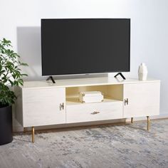 a flat screen tv sitting on top of a white entertainment center next to a potted plant