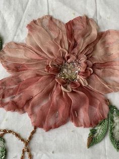 a pink flower with green leaves and beads on it's side, sitting on a piece of cloth