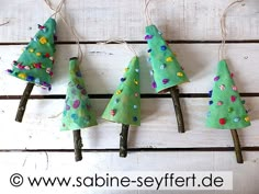 four small christmas trees are hanging from clothes pins on a white wooden background with twine