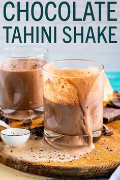 two glasses filled with chocolate tahn shake on top of a cutting board next to spoons