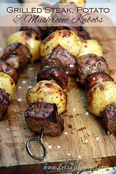 some meat and potatoes on a wooden cutting board with a metal hook in the middle