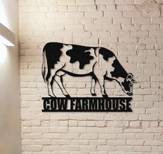 a black and white cow farm house sign on a brick wall