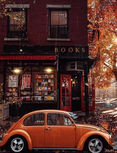 an orange vw bug parked in front of a book store with autumn leaves on the ground