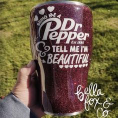 a person holding up a purple cup with writing on it in front of some grass