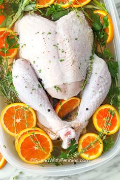 a whole chicken in a plastic container surrounded by oranges and herbs