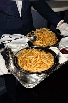 two trays filled with french fries sitting on top of a table next to silver dishes