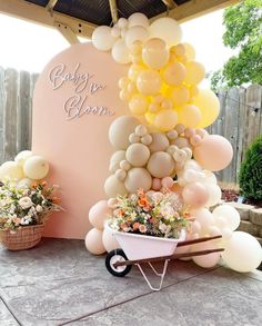 a baby shower with balloons, flowers and a wheelbarrow in front of it