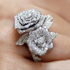 a close up of a person's hand holding a ring with two flowers on it