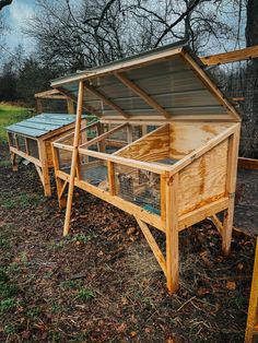 an outdoor chicken coop in the middle of a field with trees and grass behind it