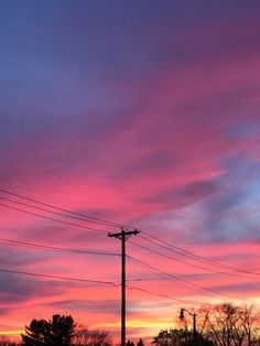 the sky is pink and blue as the sun sets in the distance behind power lines