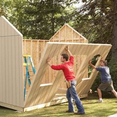 two men are building a shed in the yard with their hands on the roof and one man is reaching up