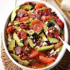 a white bowl filled with lots of different types of food next to bread on top of a table