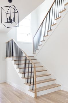 a white staircase with wooden handrails and chandelier hanging from the ceiling