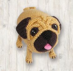 a crocheted pug dog with its tongue hanging out on a wooden floor