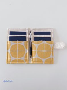 a yellow and white patterned wallet with a pen sticking out of the pocket, on a white background