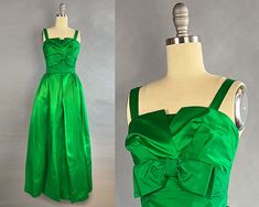 ~1950s long emerald green satin gown with bow and bustle ~Bodice comprised of a straight inner layerwith a split ruched top layer  ~Folded matte satin (cleverly using the reverse of the satin) at waistline creates belted appearance with   matte emerald bow  ~Bow with snap closure at back on waistline from which falls a beautiful bustle ~Gathering at hips and large pleats down center of skirt  ~Lined with tulle that fills out and structures the skirt  ~Metal back zipper  Size - Small, Extra Small Green Satin Gown With Pleated Bodice, Green Satin Evening Gown, Vintage Fitted Green Gown, Vintage Green Gown For Wedding, Vintage Green Wedding Gown, Green Silk Formal Gown, 1950s Style Green Formal Dress, Green 1950s Style Formal Dress, Green Satin Gown