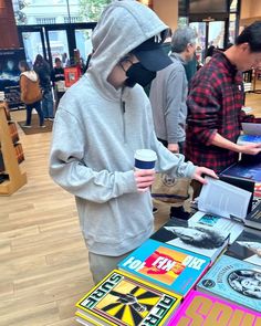 a man wearing a mask standing in front of a table with records on it and holding a coffee cup