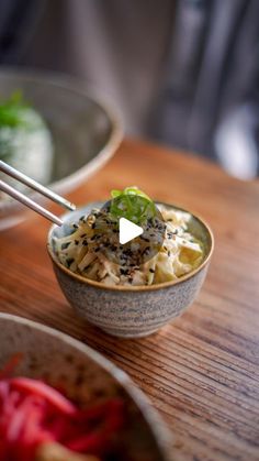 a bowl of noodles with chopsticks in it sitting on a table next to another bowl