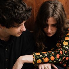 a man and woman sitting next to each other looking at something on the table in front of them