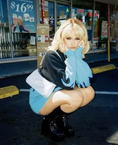 a woman in short skirt and boots sitting on the ground next to a store front