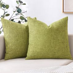 two green pillows sitting on top of a white couch next to a potted plant