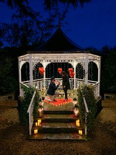 two people standing on steps in front of a gazebo at night with candles lit