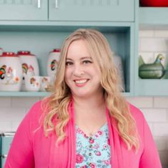 a woman standing in front of a kitchen counter with dishes on the shelves behind her