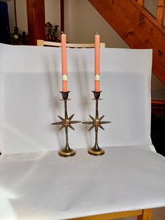 two candles sitting on top of a table next to a white sheet and some stairs