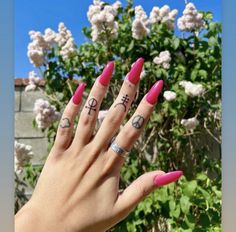 a woman's hand with pink fingernails and tattoos on her fingers, in front of some flowers