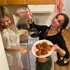 two girls in the kitchen preparing food on a plate and one girl is holding a spoon