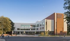 an office building with people walking around the front entrance and parking lot in front of it