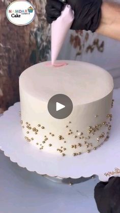 a person decorating a cake with white frosting and gold sprinkles