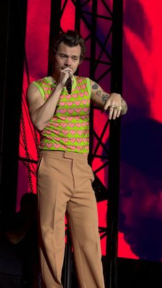 a man standing on top of a stage with a microphone in his hand and wearing brown pants