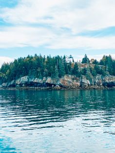 an island in the middle of water with trees on it's sides and blue sky above