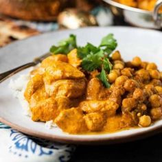 a white plate topped with chicken and chickpeas covered in sauce next to other dishes