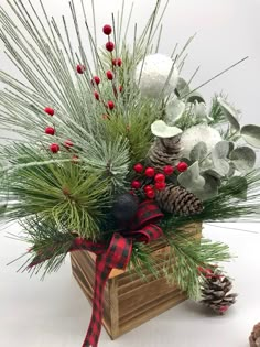 a christmas arrangement with pine cones, berries and greenery in a wooden box on a white background