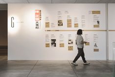 a person walking in front of a white wall with posters on it and writing on the walls