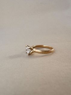 a gold ring with a single diamond on the top, sitting on a plain surface