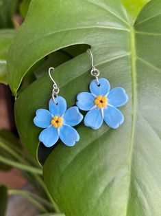 small blue flowers are hanging from silver earwires on a green leafy plant